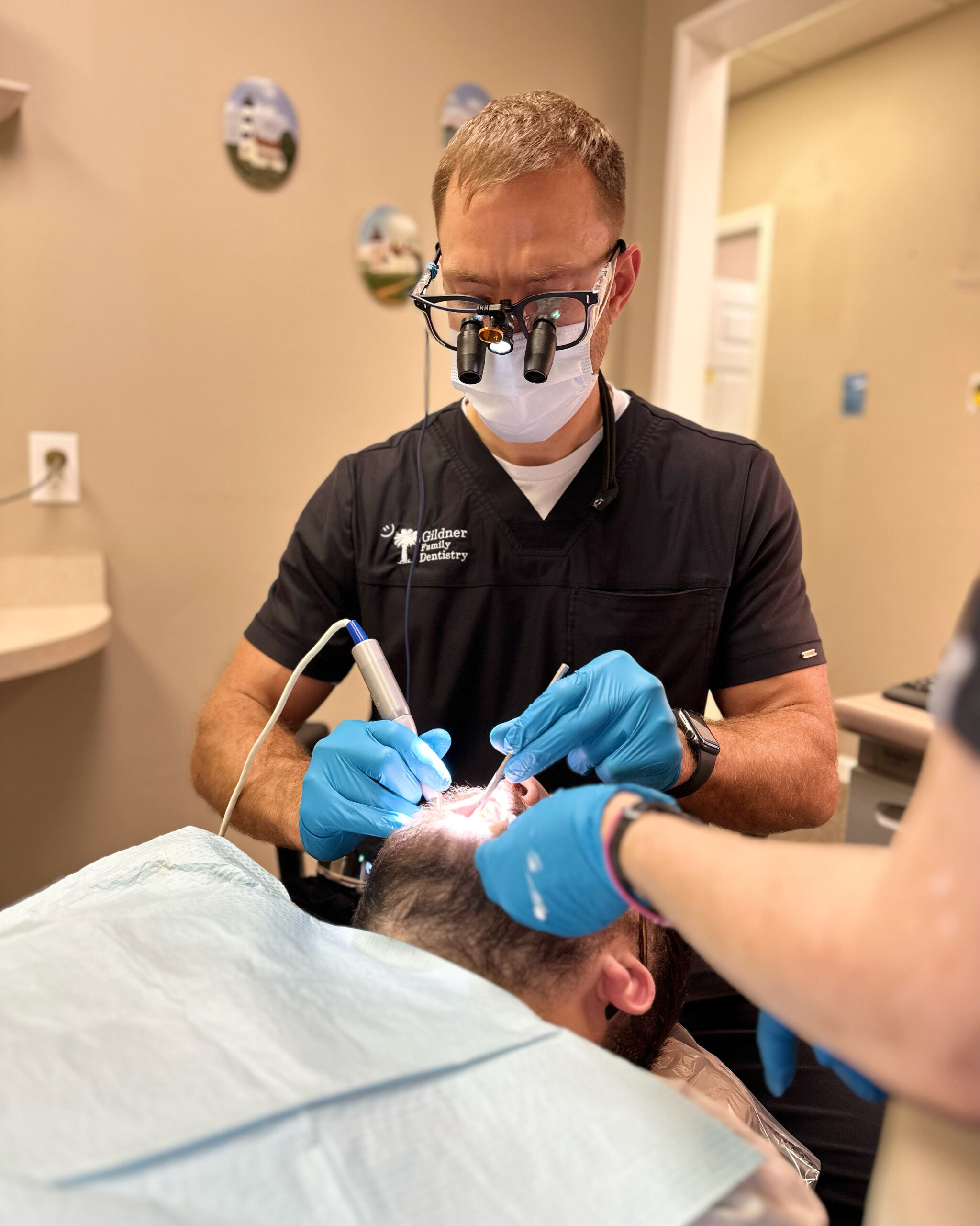 Dr. Robert Gildner , wearing a blue shirt and tie,from Gildner Family Dentistry sitting in a dental chair with his hands on his knees